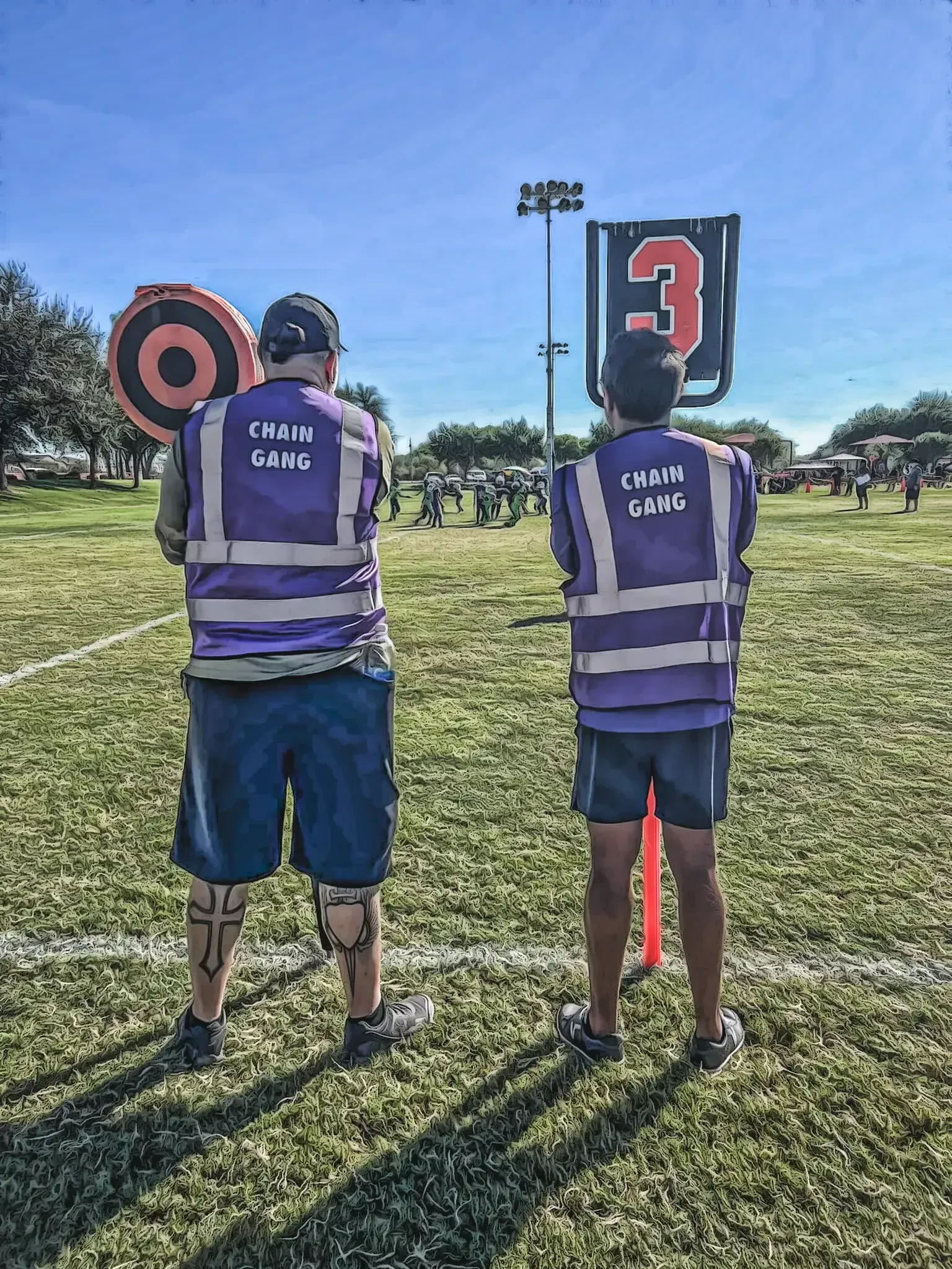 Two workers in purple safety vests stand on grass facing target signs at an outdoor training range.