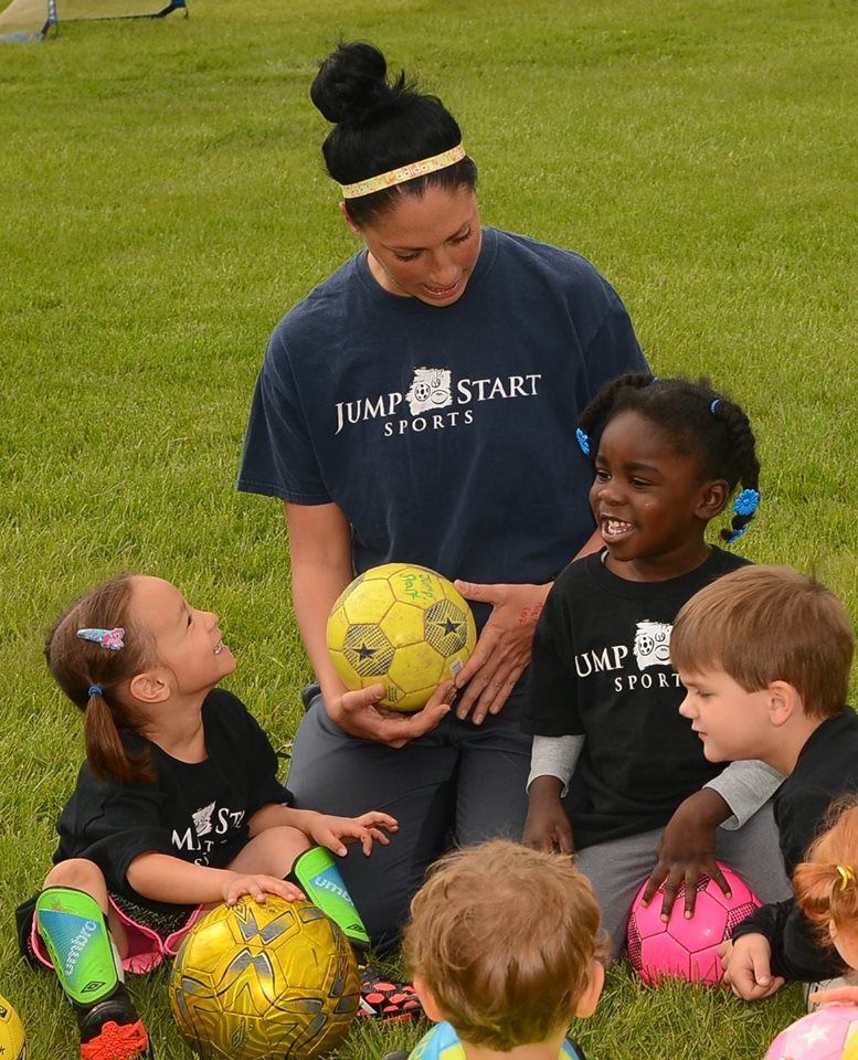 A woman wearing a jump start shirt is holding a soccer ball