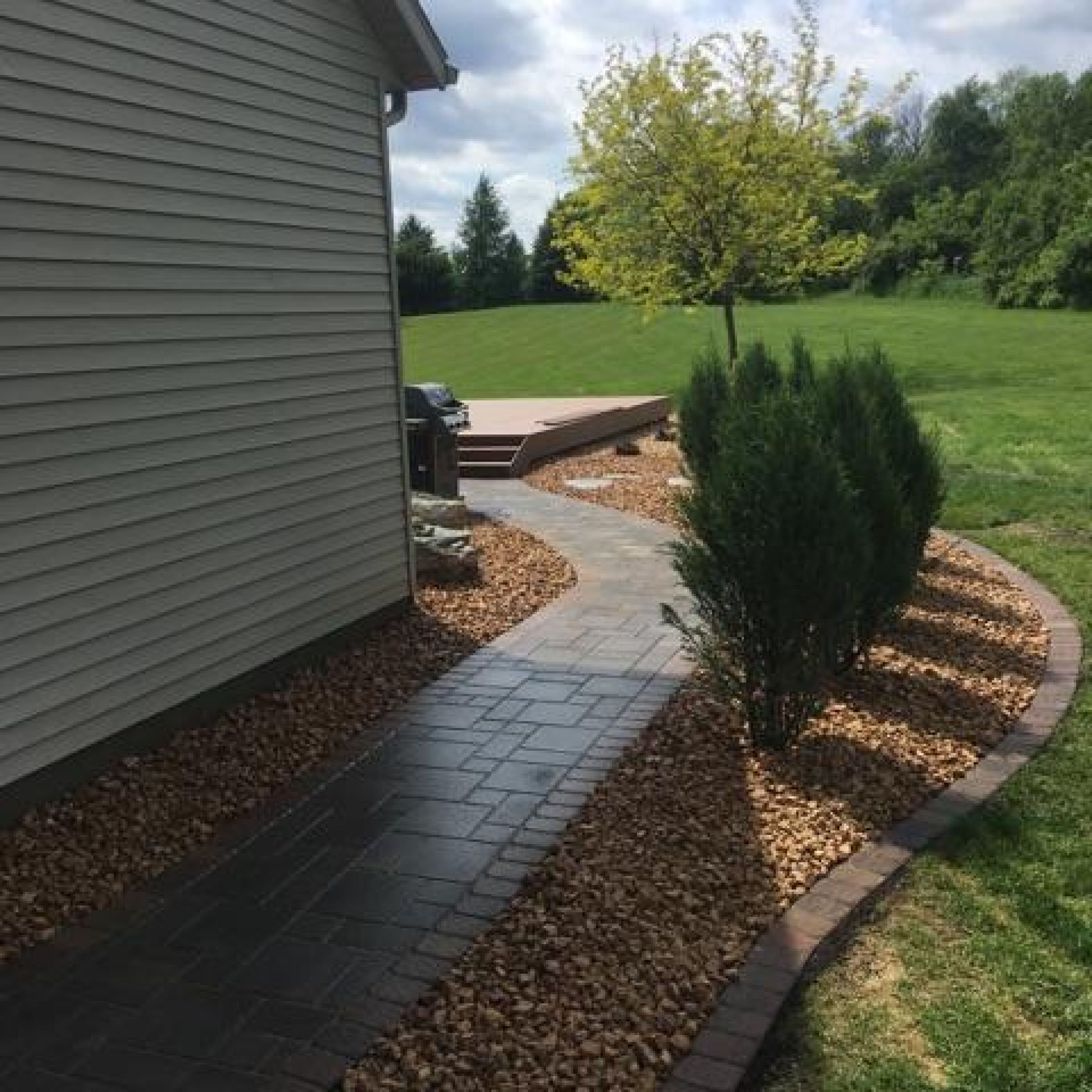A brick walkway leading to a house and a deck.