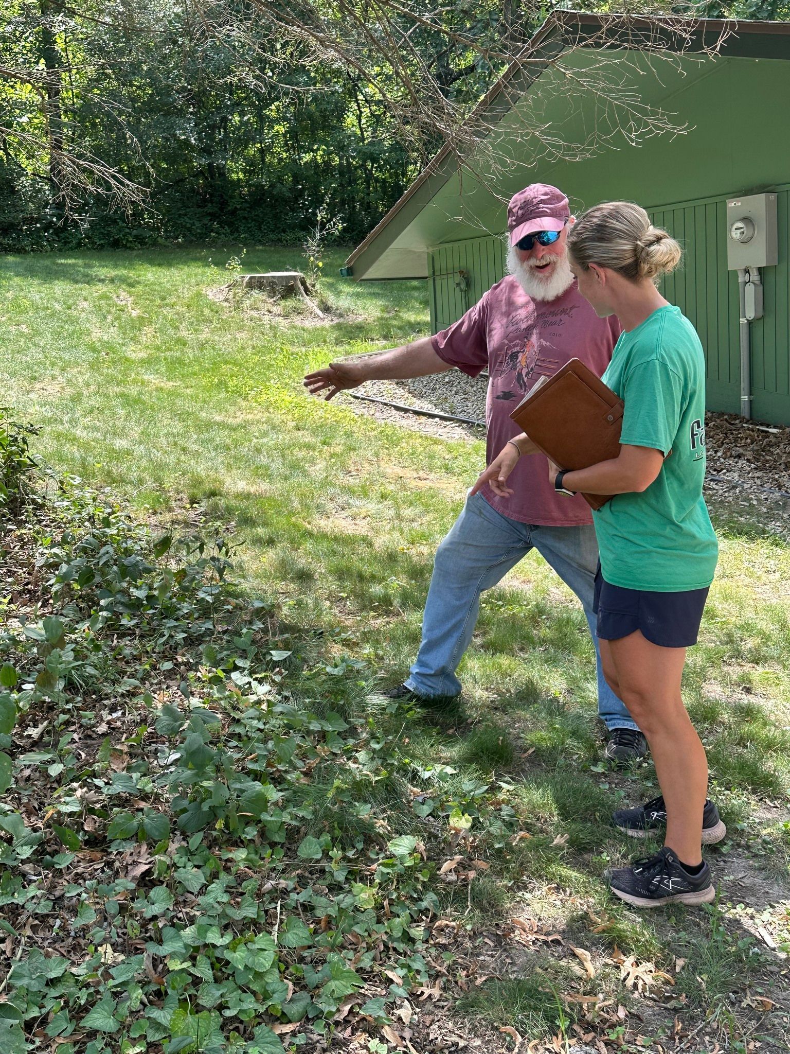 A man and a woman are standing in the grass looking at a plant.