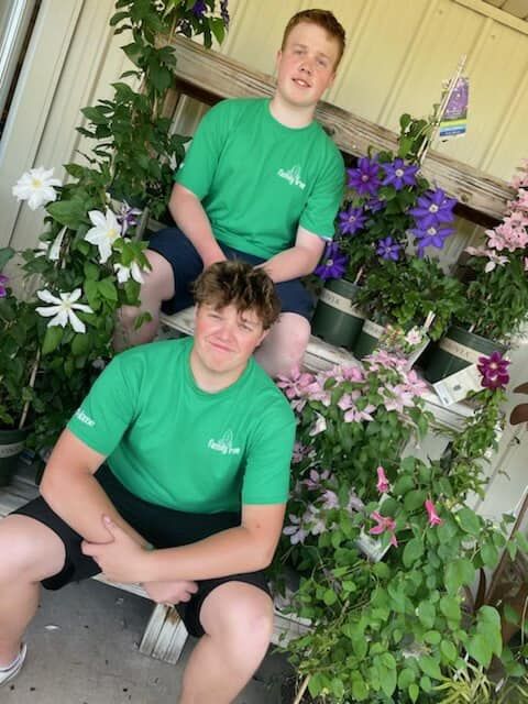 Two boys in green shirts are sitting on a bench surrounded by flowers