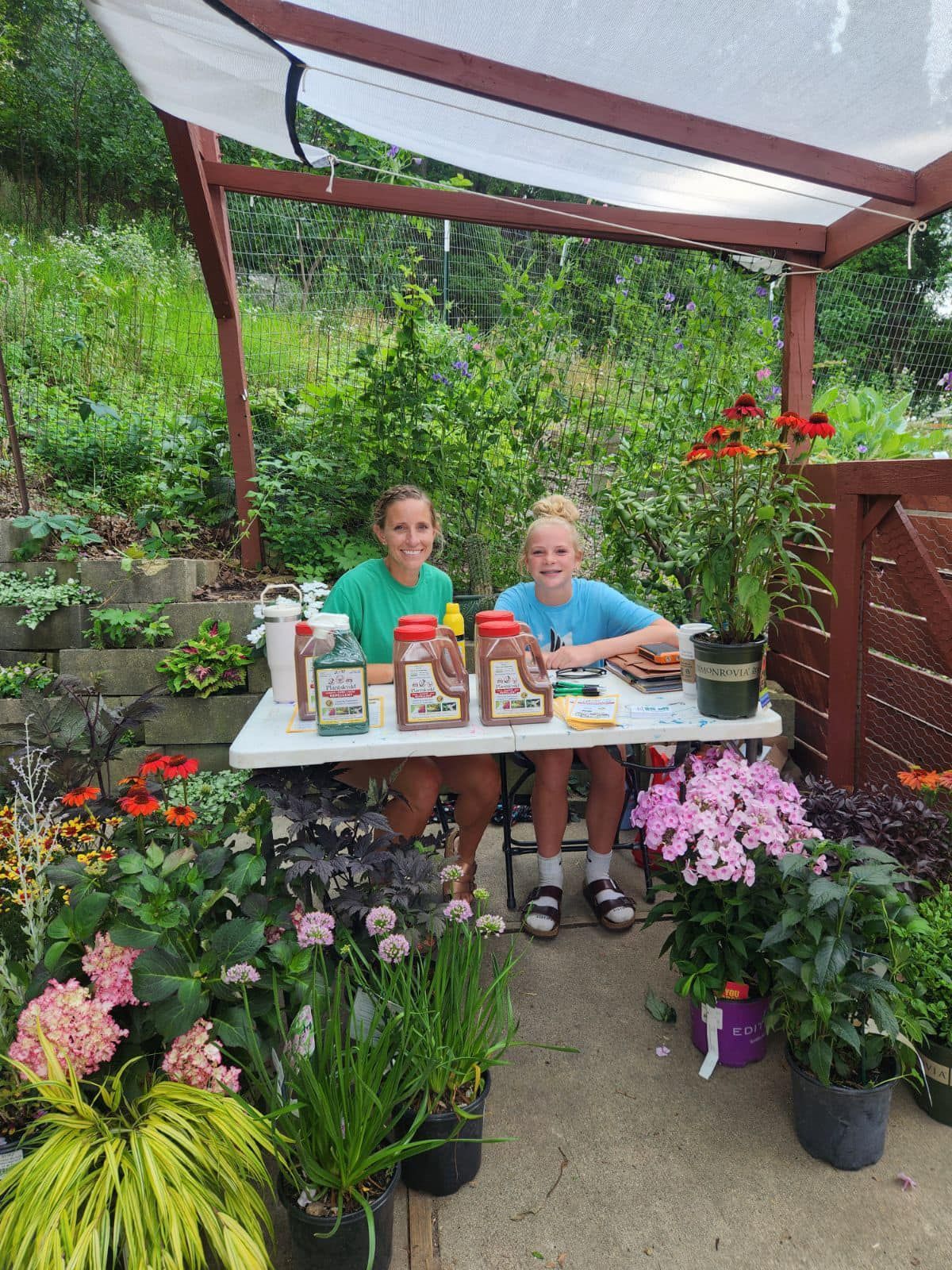 Two young girls are sitting at a table surrounded by potted plants.
