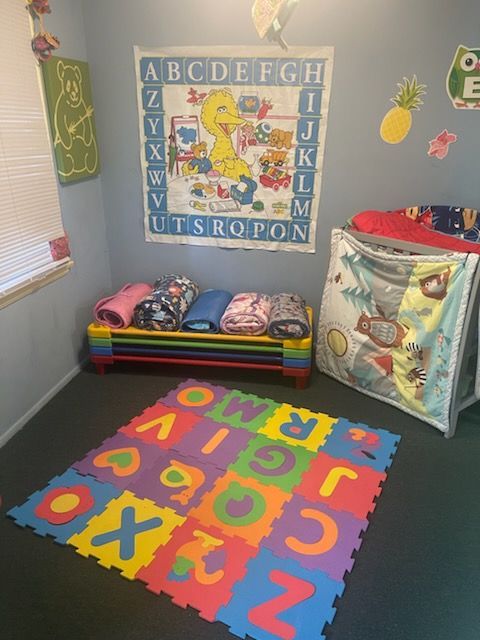 Playroom with alphabet rug, colorful bench with blankets, alphabet banner, and play tent.