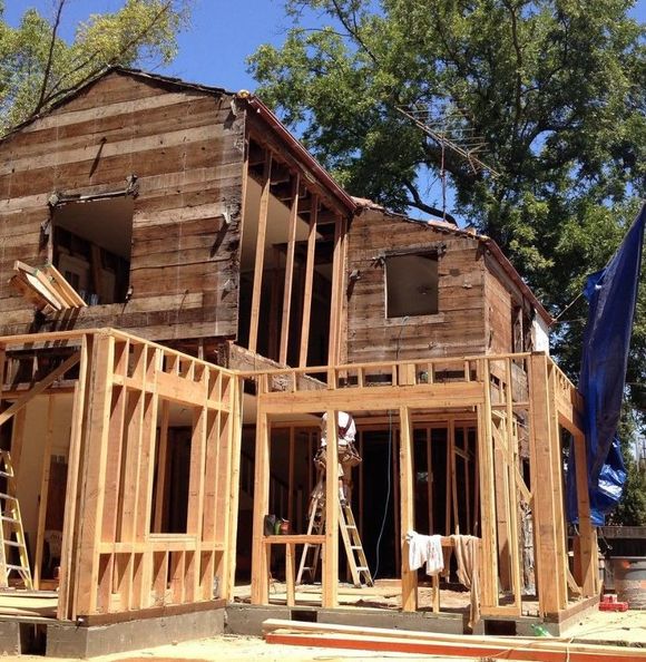 A wooden house is being built with a blue tarp in front of it