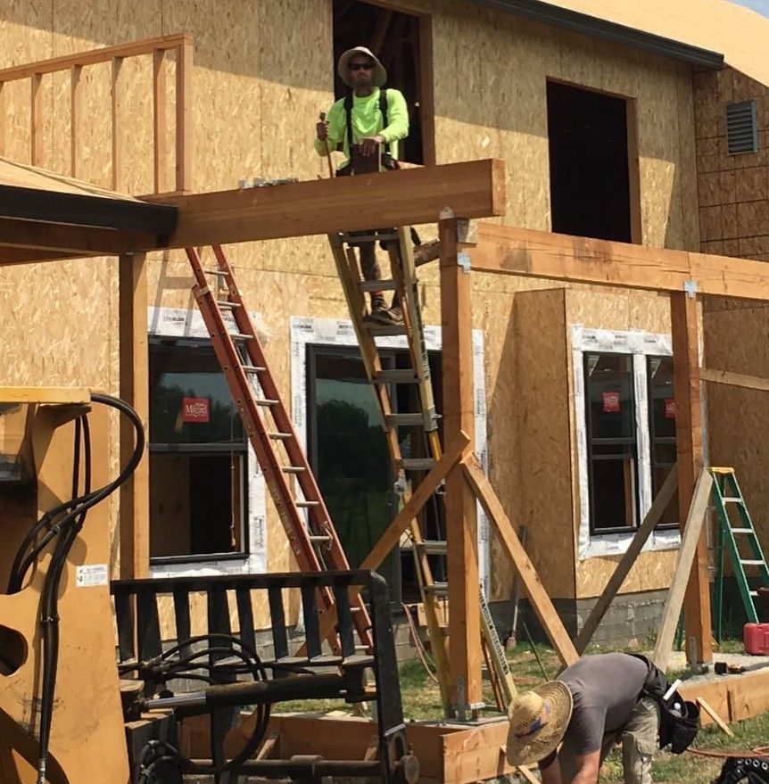 A man is standing on a ladder in front of a house under construction