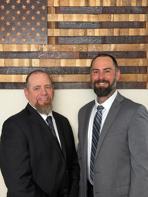 Two men in suits and ties are standing in front of an american flag.