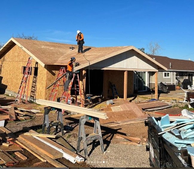 A wooden house is being built with a blue tarp in front of it