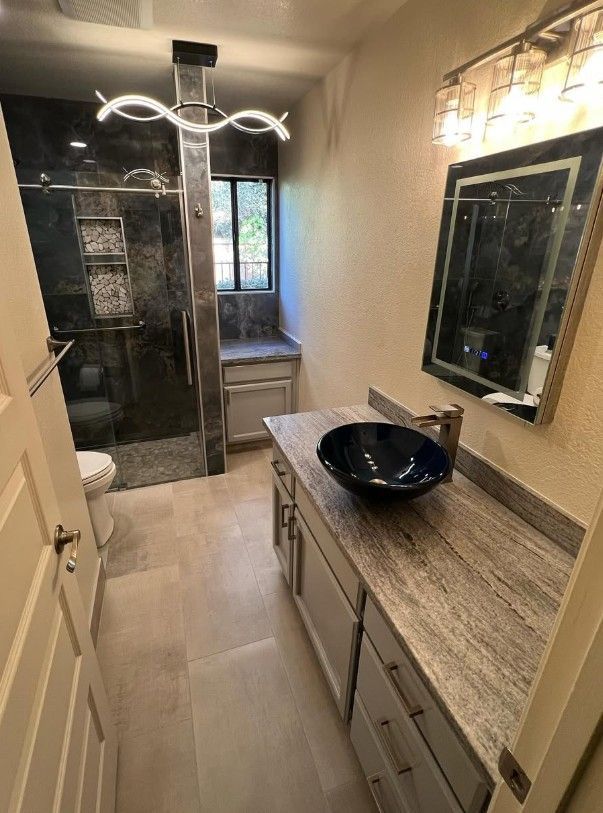 A bathroom with a sink , mirror , toilet and shower.