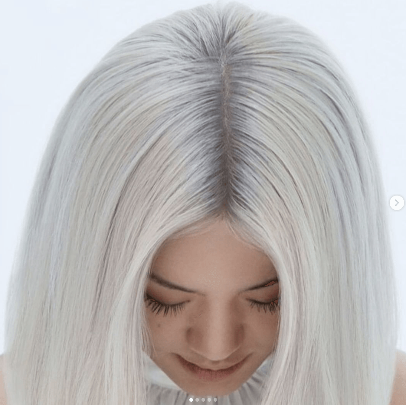 A woman with long white hair is smiling with her eyes closed.