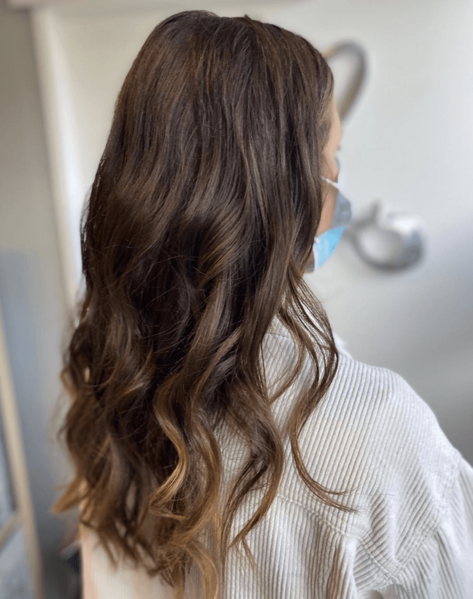 A woman with long brown hair is wearing a mask.