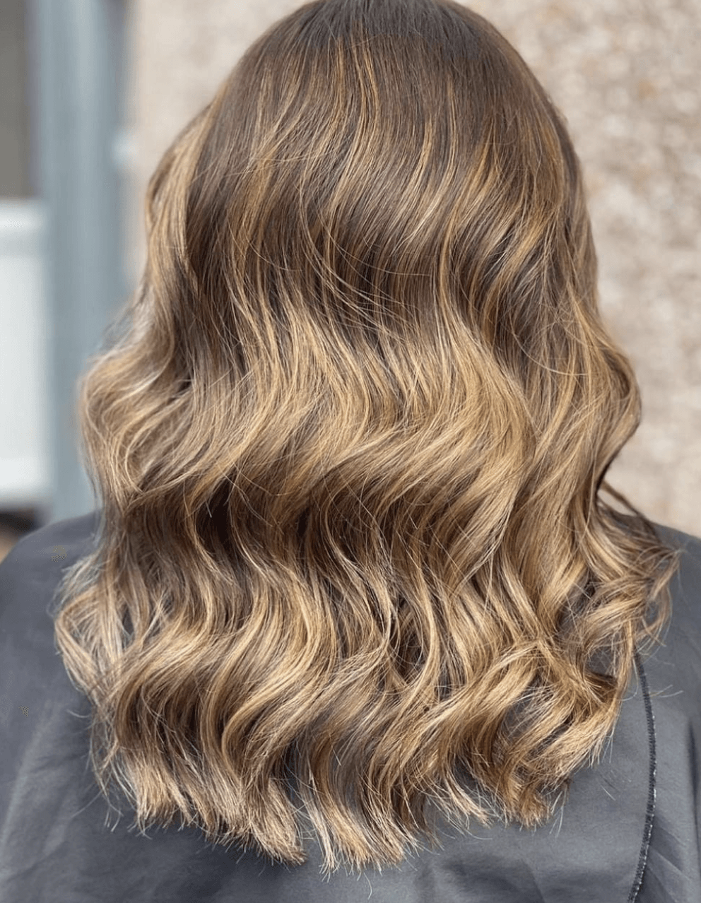 A woman with long wavy brown hair is wearing a black cape.