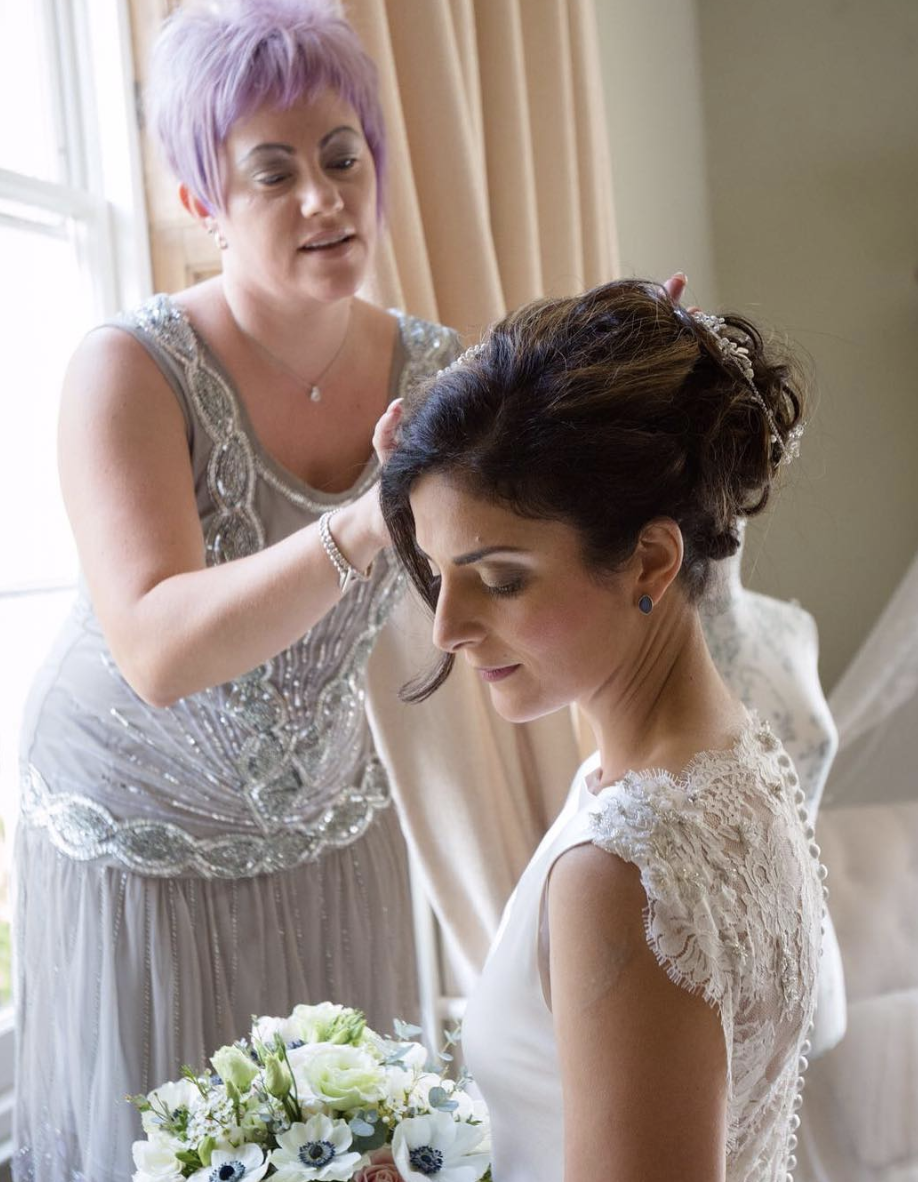 A woman with purple hair is helping a bride with her hair