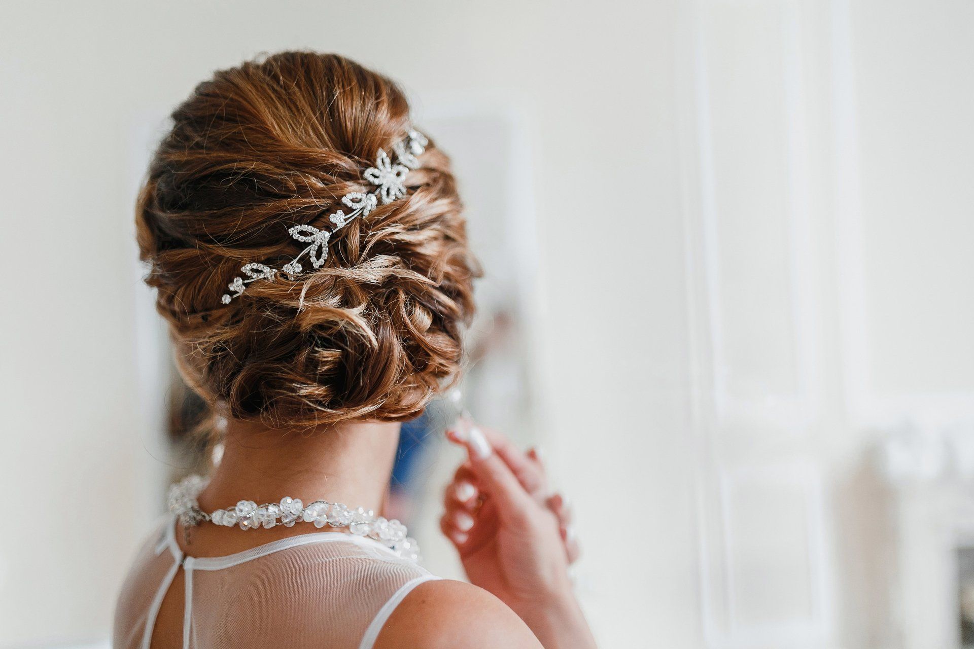 A woman in a wedding dress is looking at her hair in the mirror.