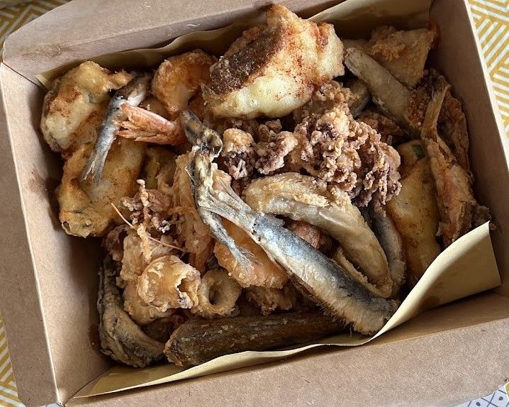 Mix di frutti di mare fritti in una scatola di cartone: pesce, calamari, gamberi e patate.