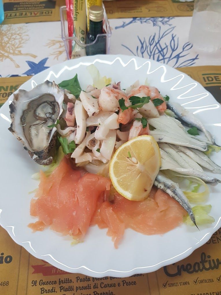 Piatto di frutti di mare: ostriche, salmone affumicato, gamberi, calamari, acciughe, fetta di limone su piatto bianco.