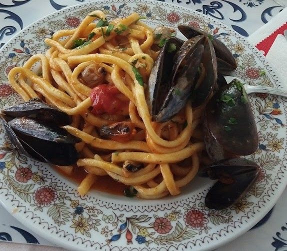 Pasta con cozze in salsa di pomodoro, servita su un piatto decorato con motivi floreali.