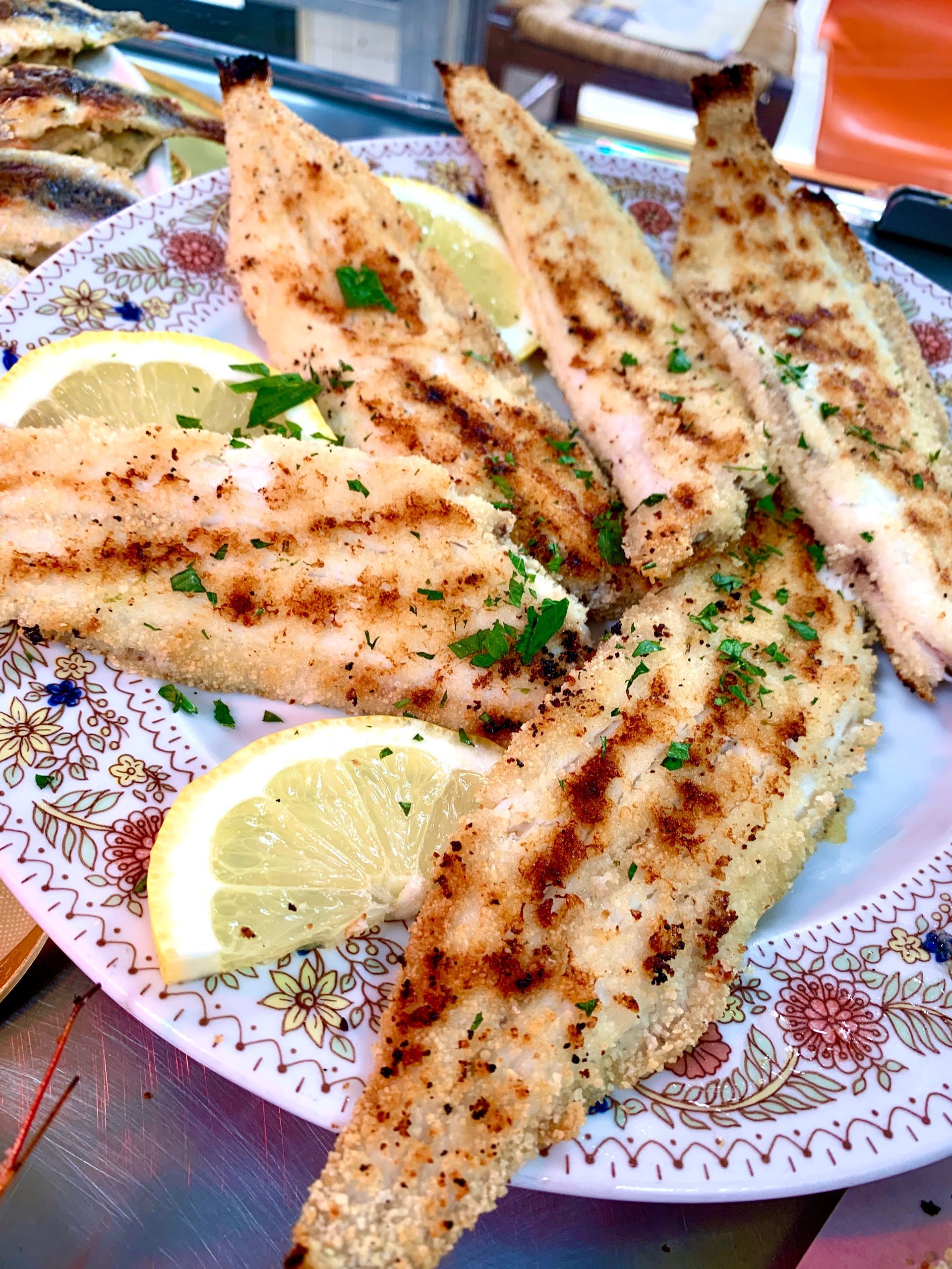 Filetti di pesce grigliati su un piatto decorato, guarnito con fette di limone e prezzemolo.