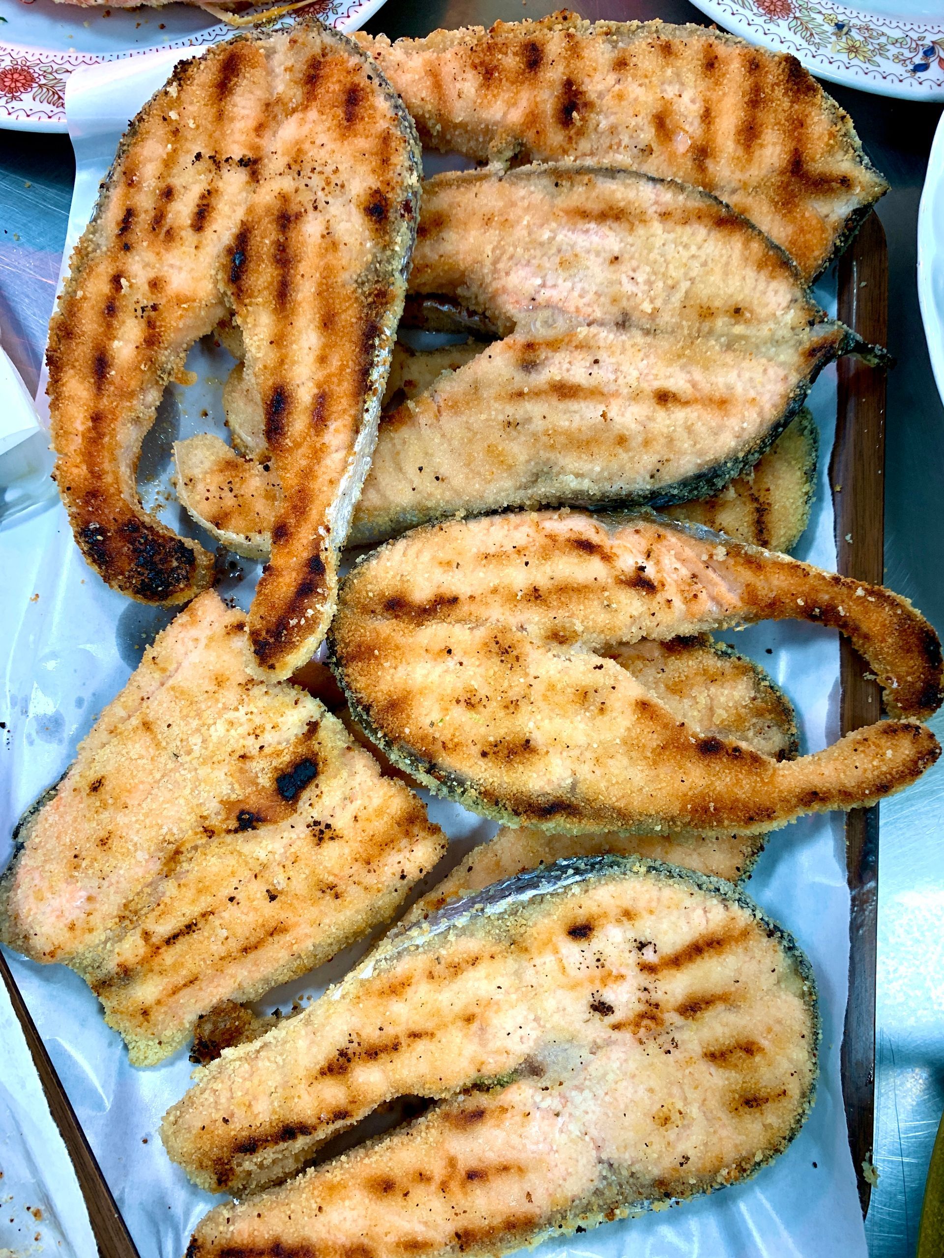 Tranci di salmone grigliati disposti su una superficie bianca, con i segni della griglia e un colore arancione chiaro.