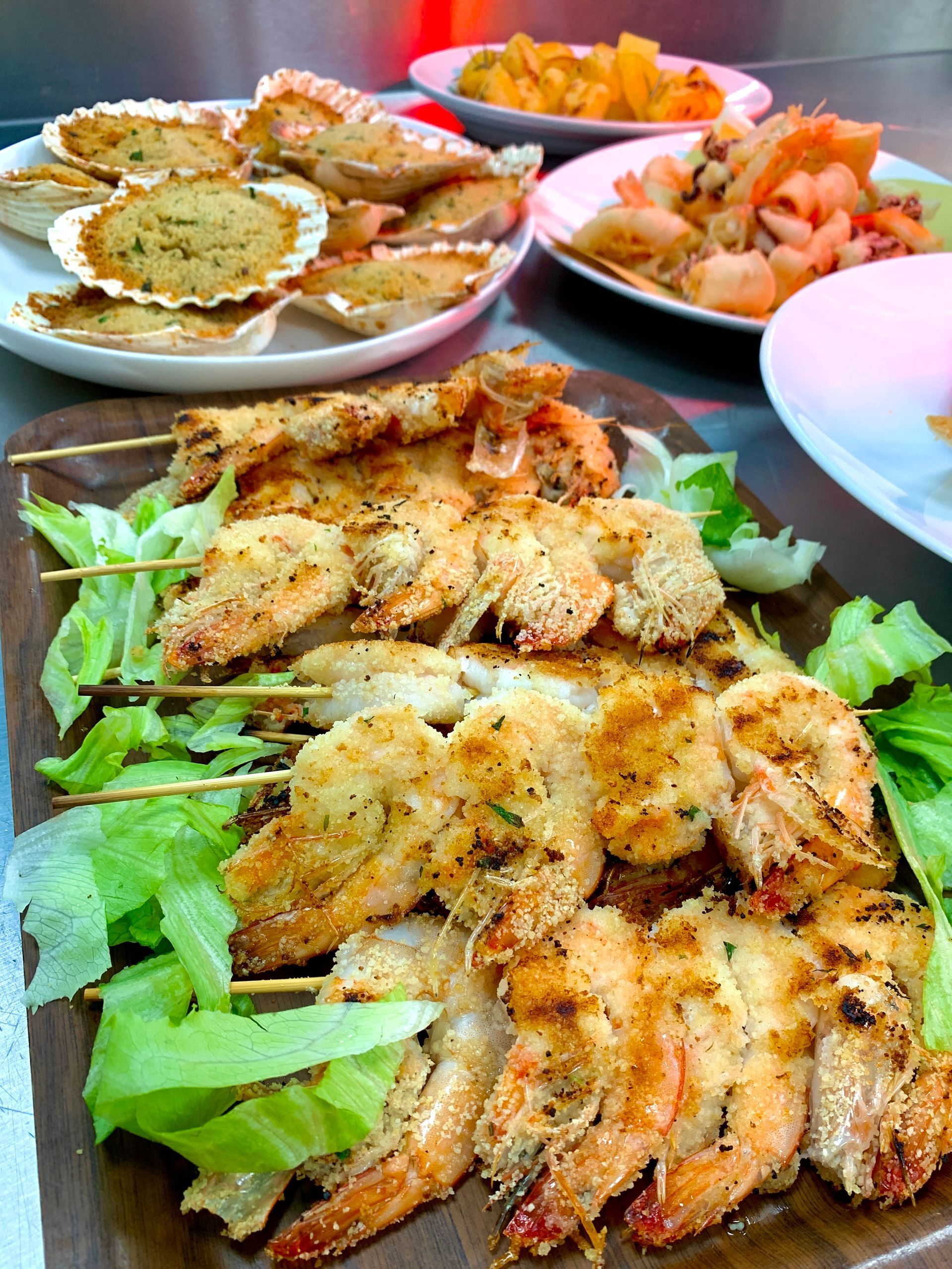 Spiedini di gamberi alla griglia su un letto di lattuga, con altri piatti di pesce nei piatti.