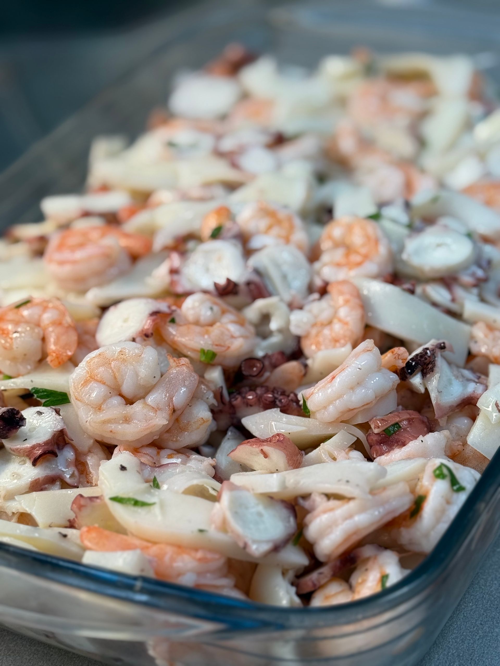 Insalata di mare con gamberi, polpo e calamari in un piatto di vetro trasparente, primo piano.