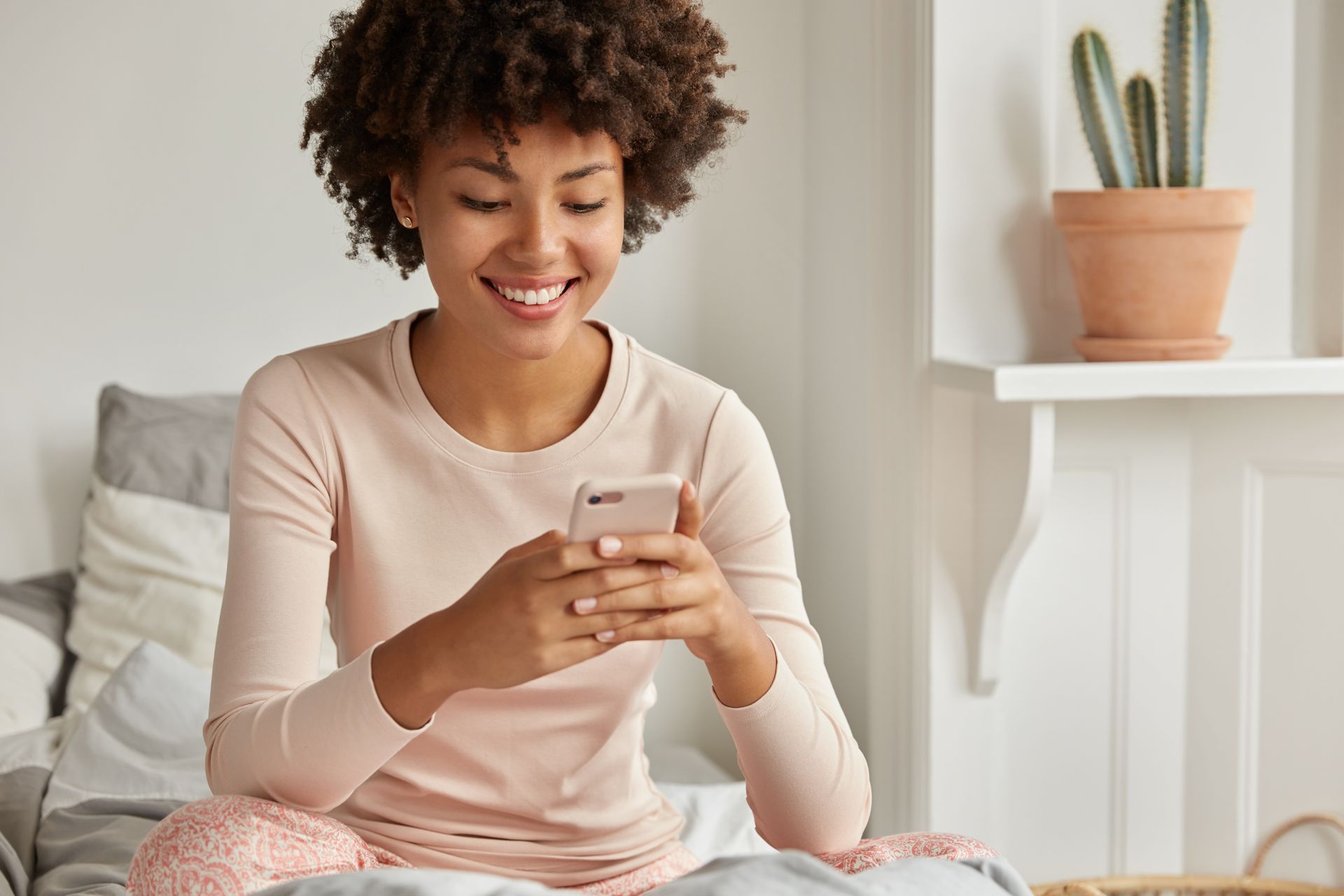 A woman is sitting on a bed looking at her cell phone.