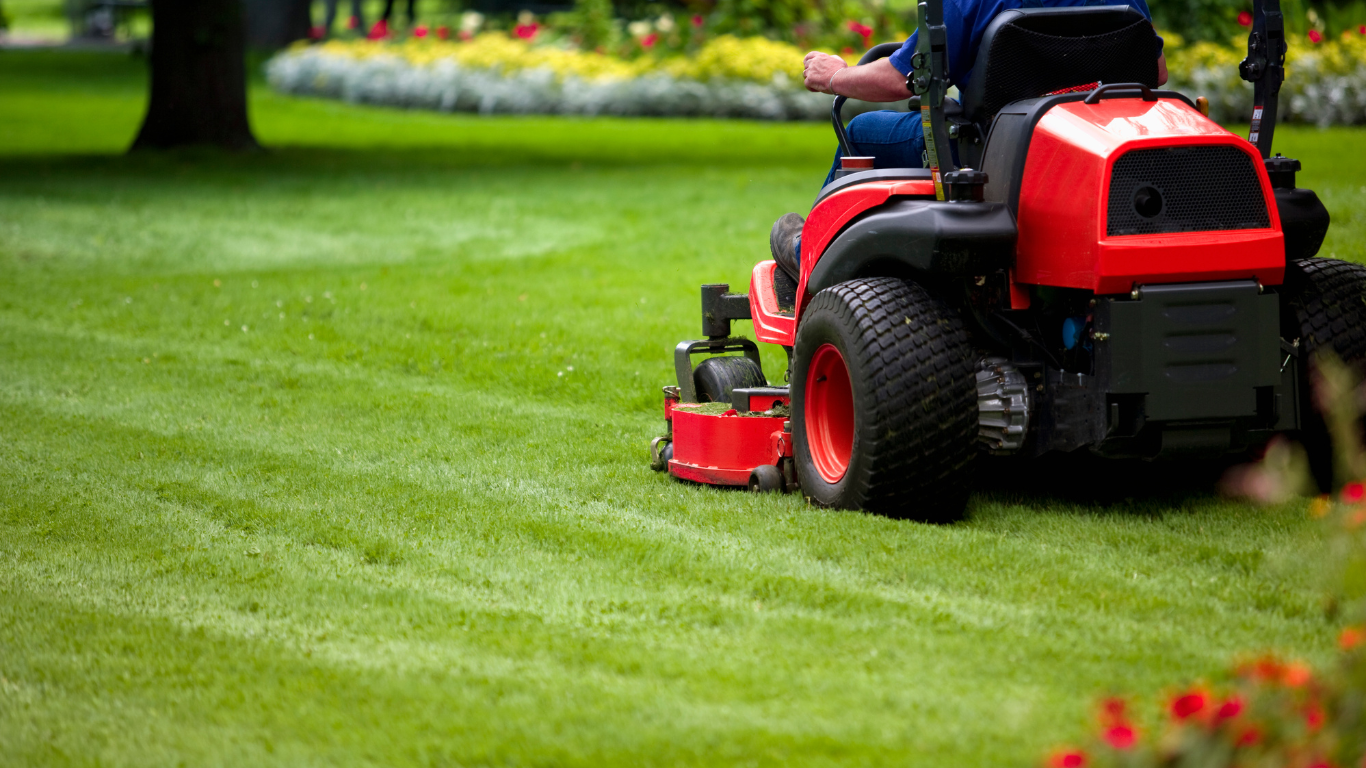 A man is riding a lawn mower on a lush green lawn.