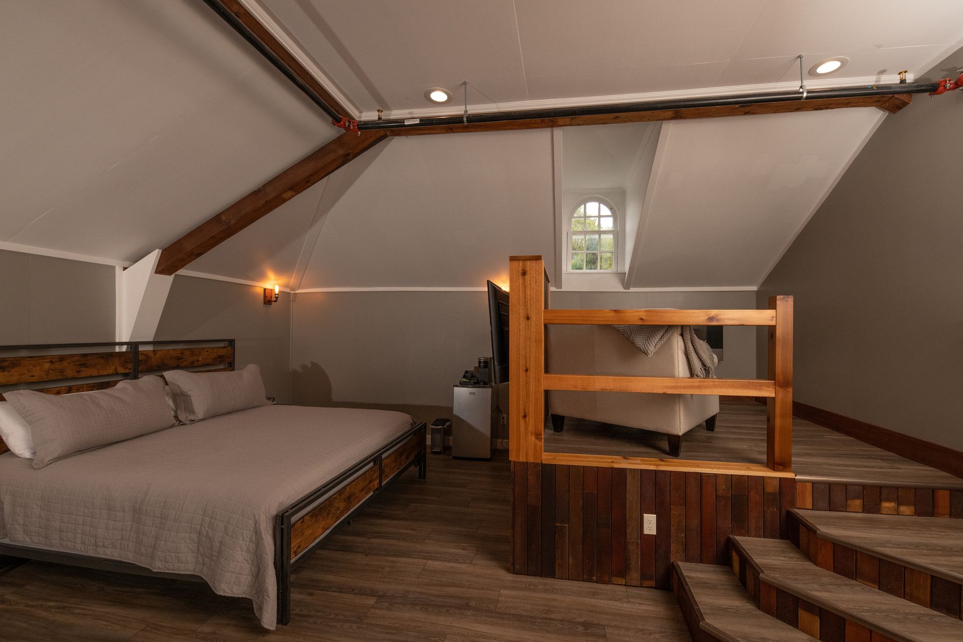 A bedroom with a bed , stairs and a couch.