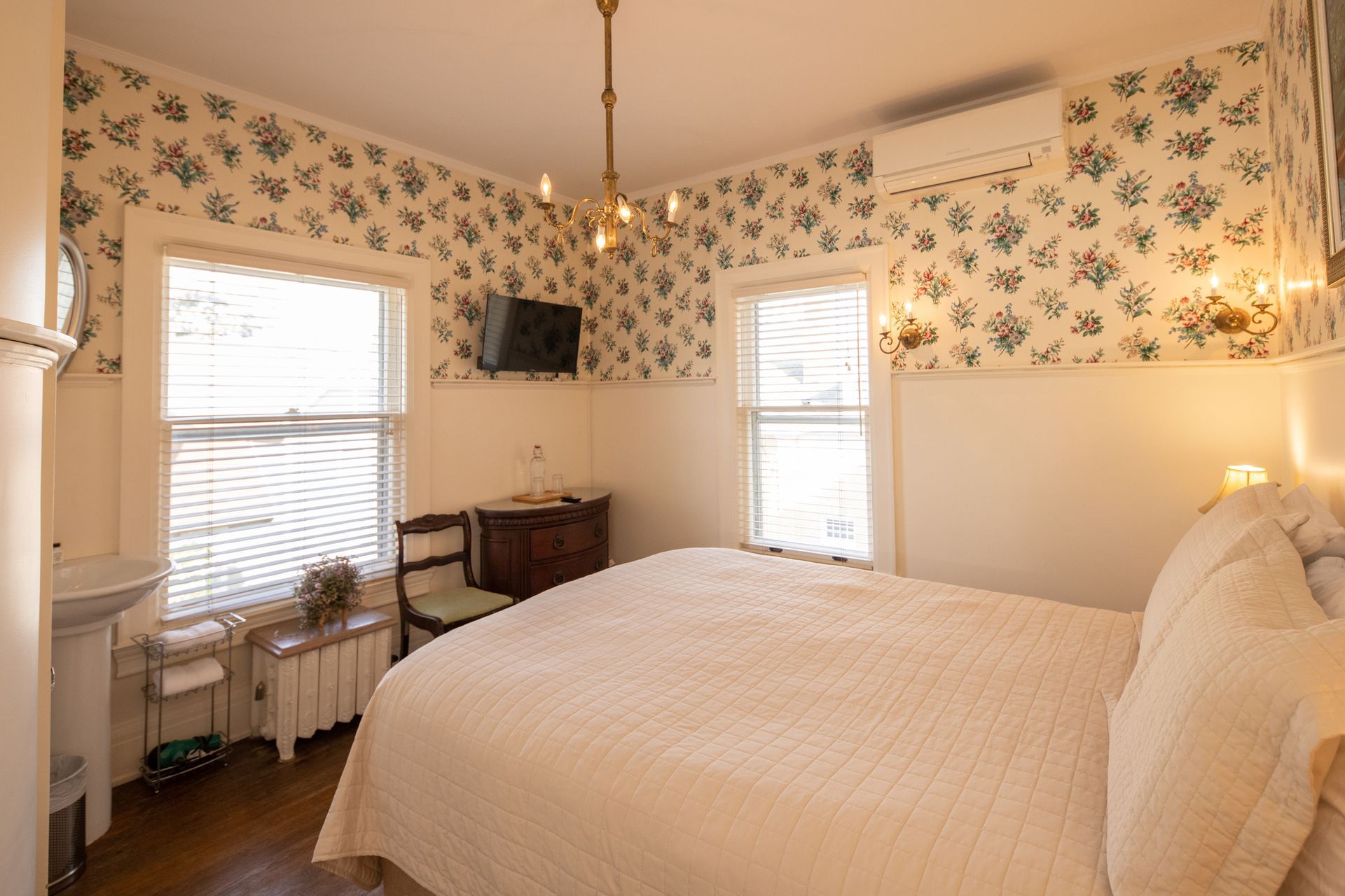 A bedroom with a bed , two windows , a sink and a television.