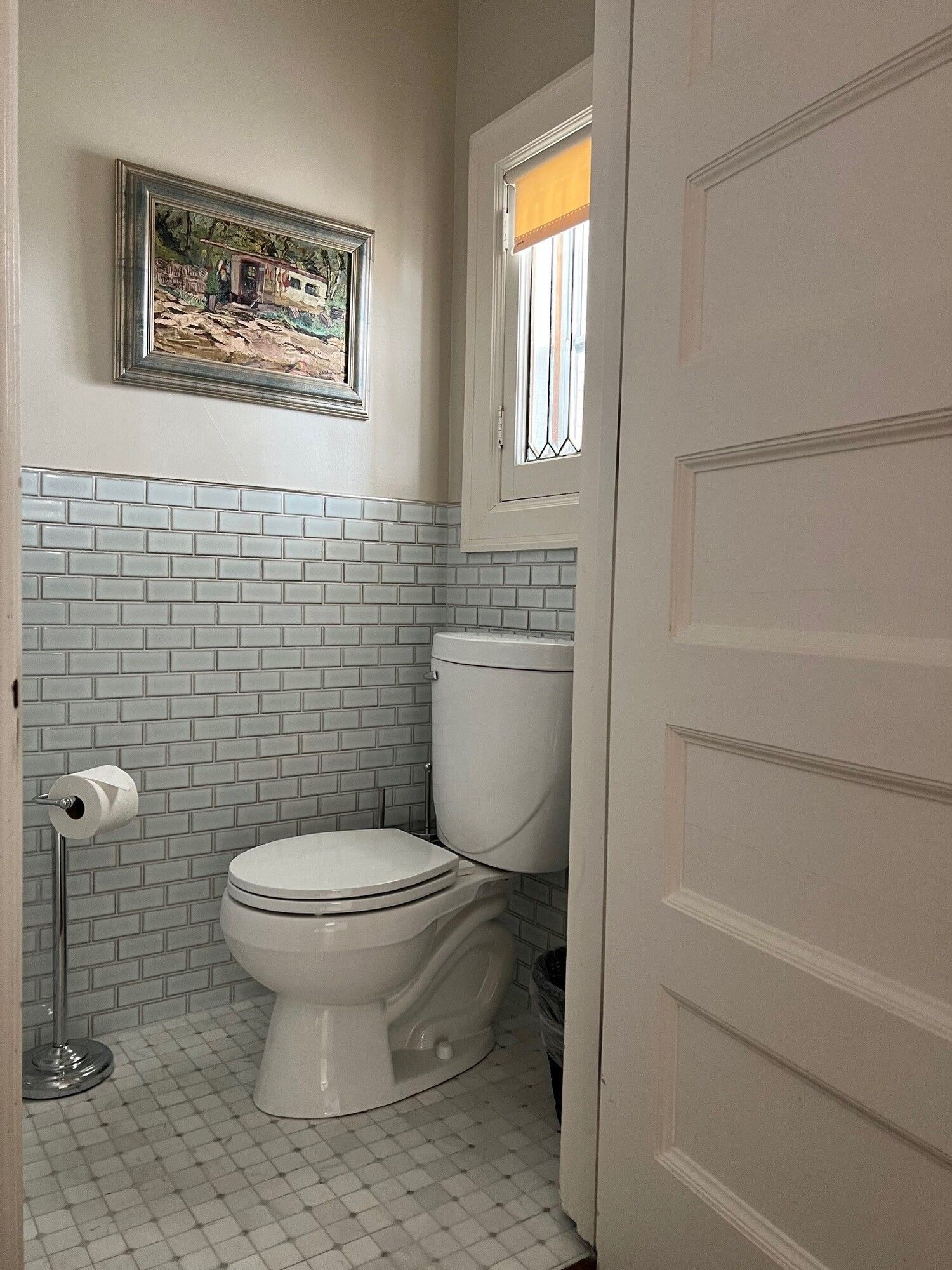A bathroom with a toilet and a painting on the wall.