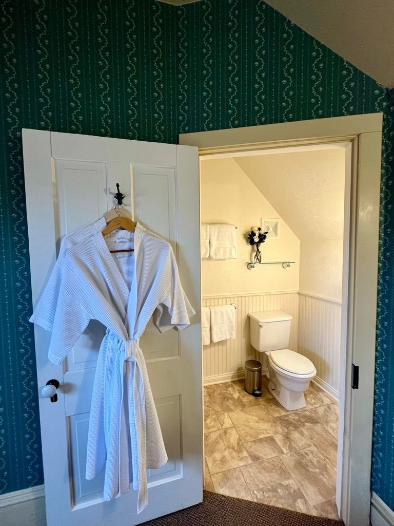 A bathrobe is hanging on a door in a bathroom next to a toilet.