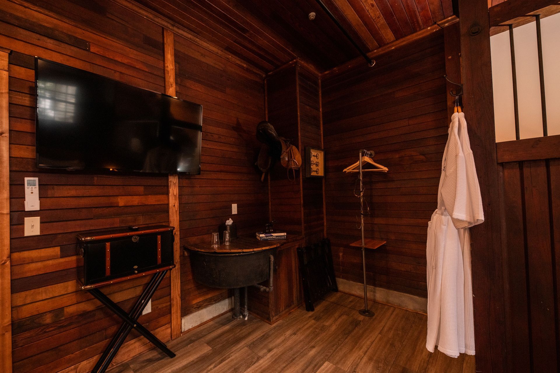 A wooden room with a flat screen tv and a white robe hanging on the wall.