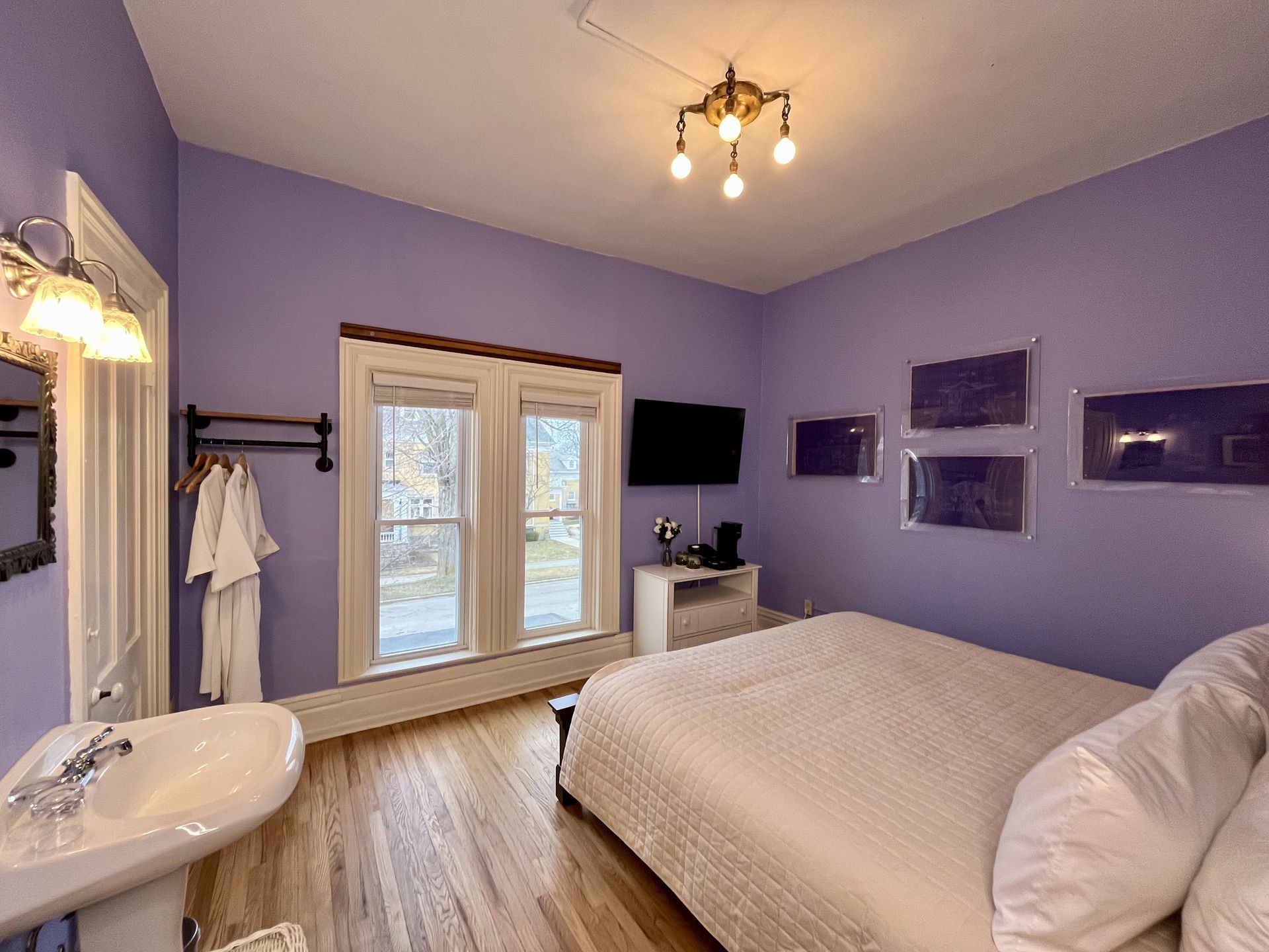 A bedroom with purple walls , a bed , a sink and a television.