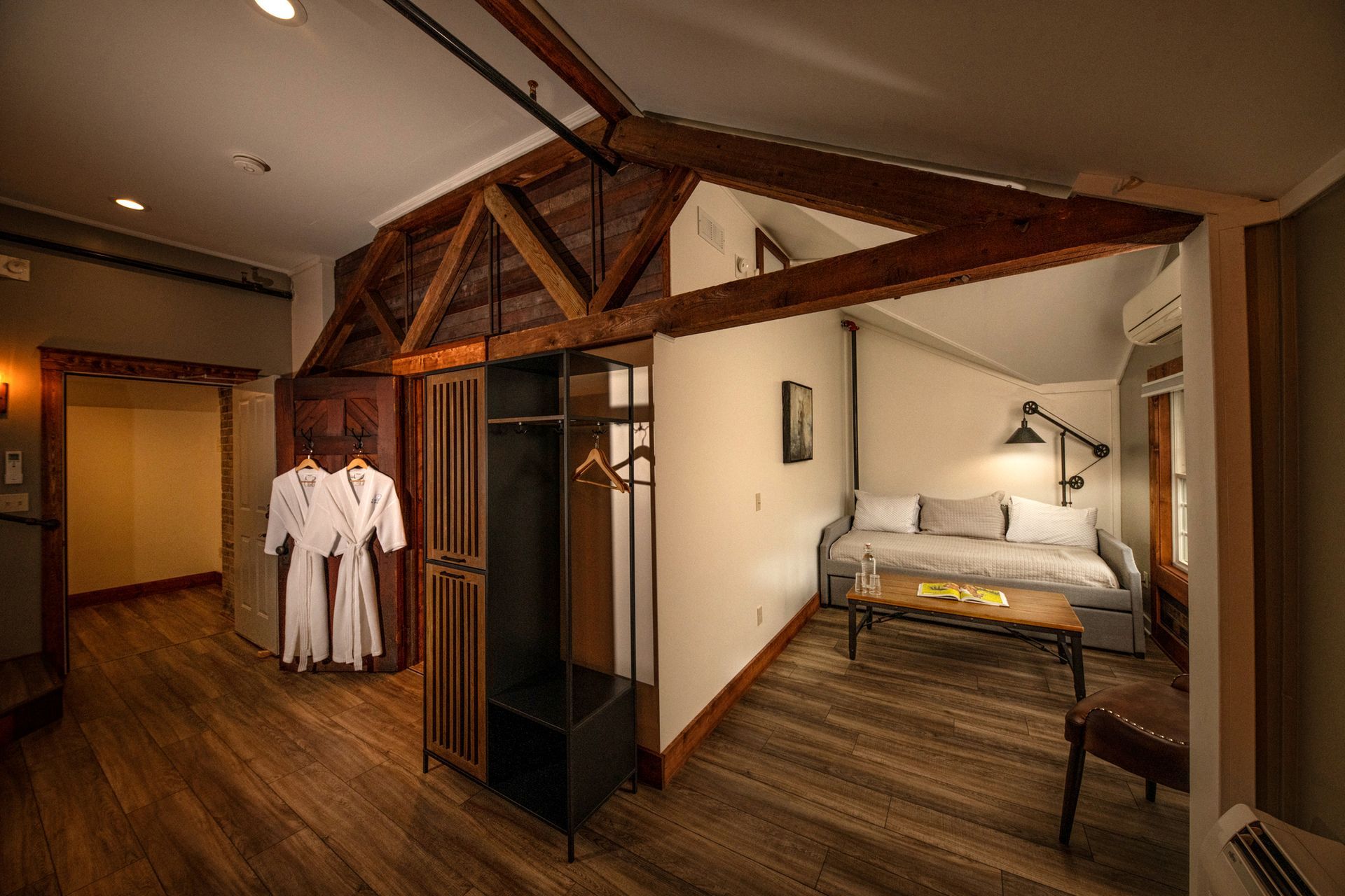 A hotel room with a couch and robes hanging on the wall.