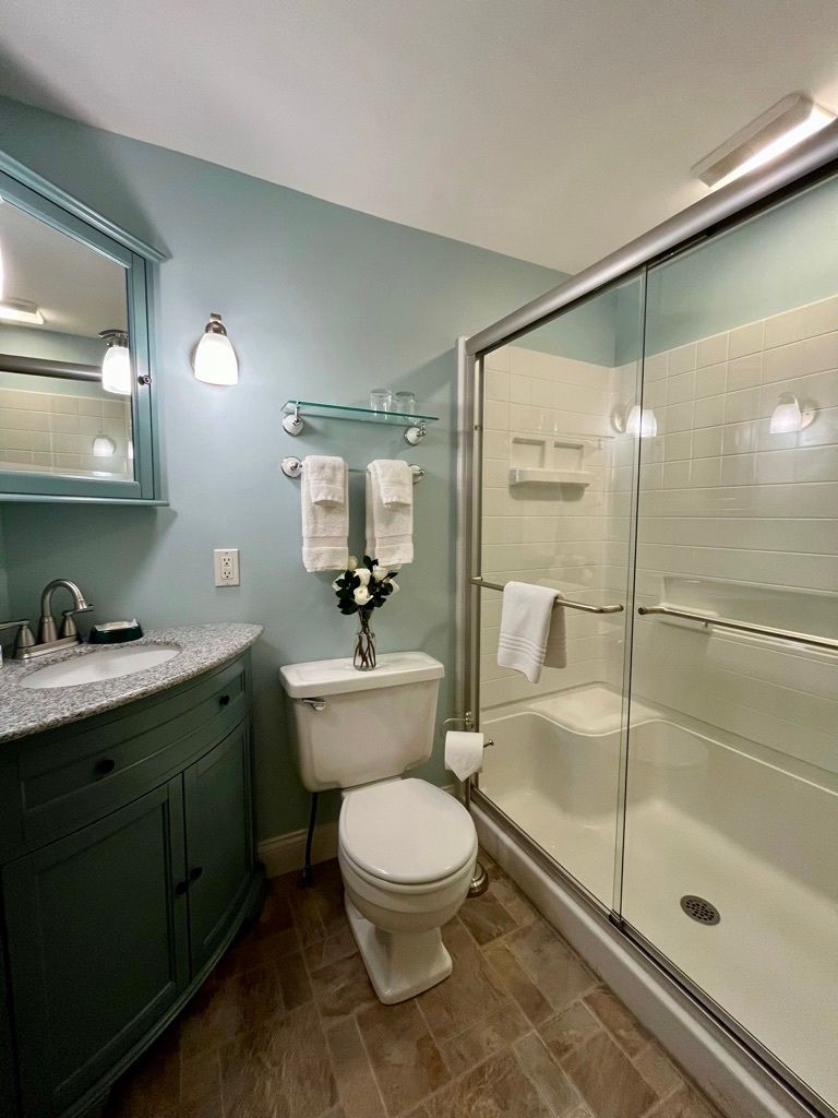 A bathroom with a toilet , sink , mirror and shower.