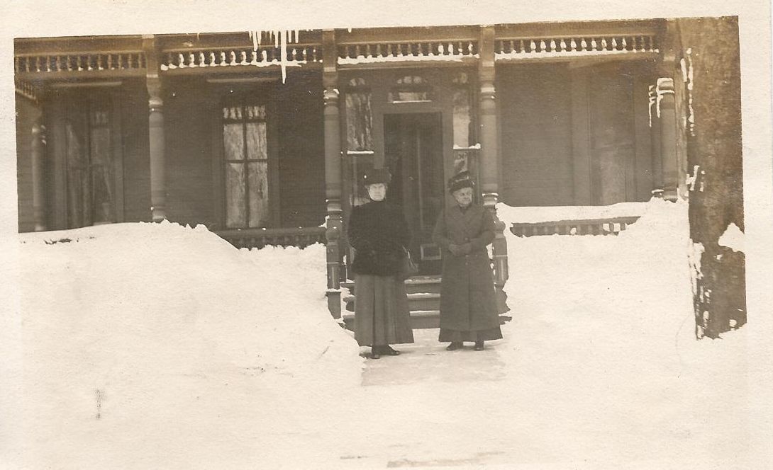 Two people are standing in front of a house in the snow