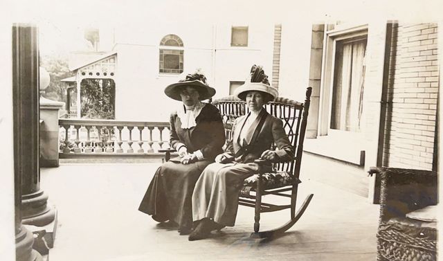 Two women are sitting in rocking chairs on a porch.