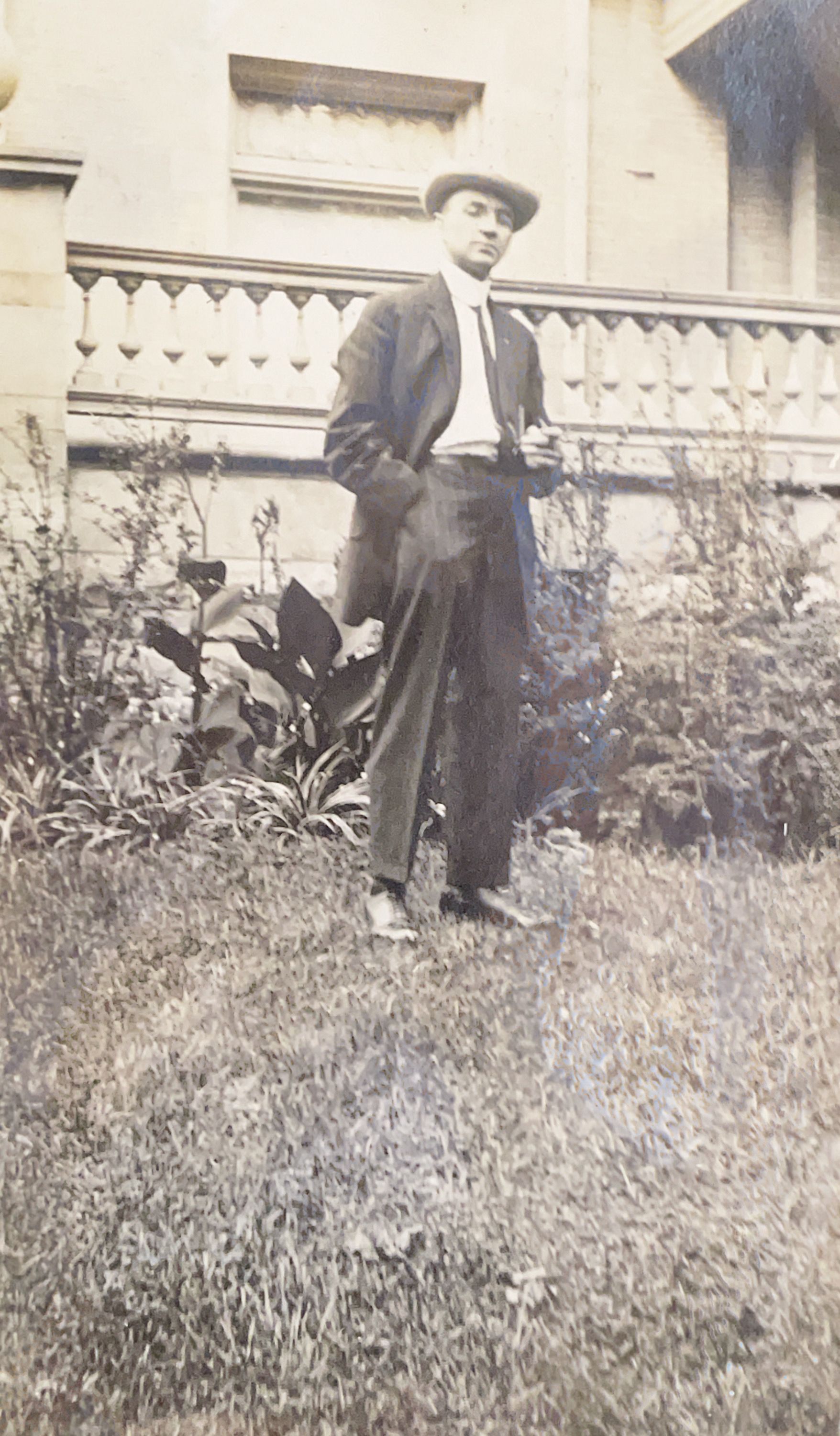 A man in a suit and hat is standing in the grass holding a cane.