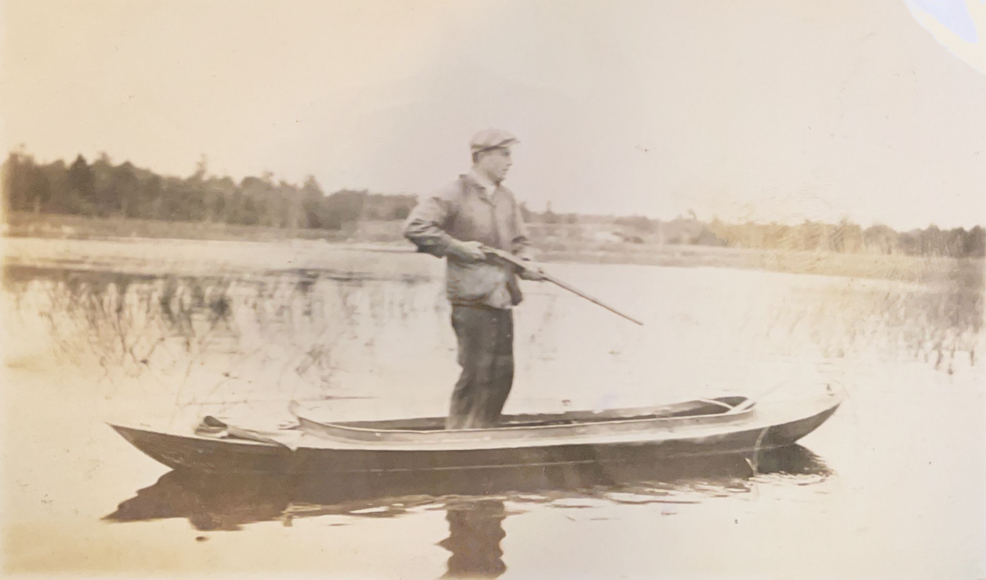 A man is standing in a boat in the water holding a fishing rod.