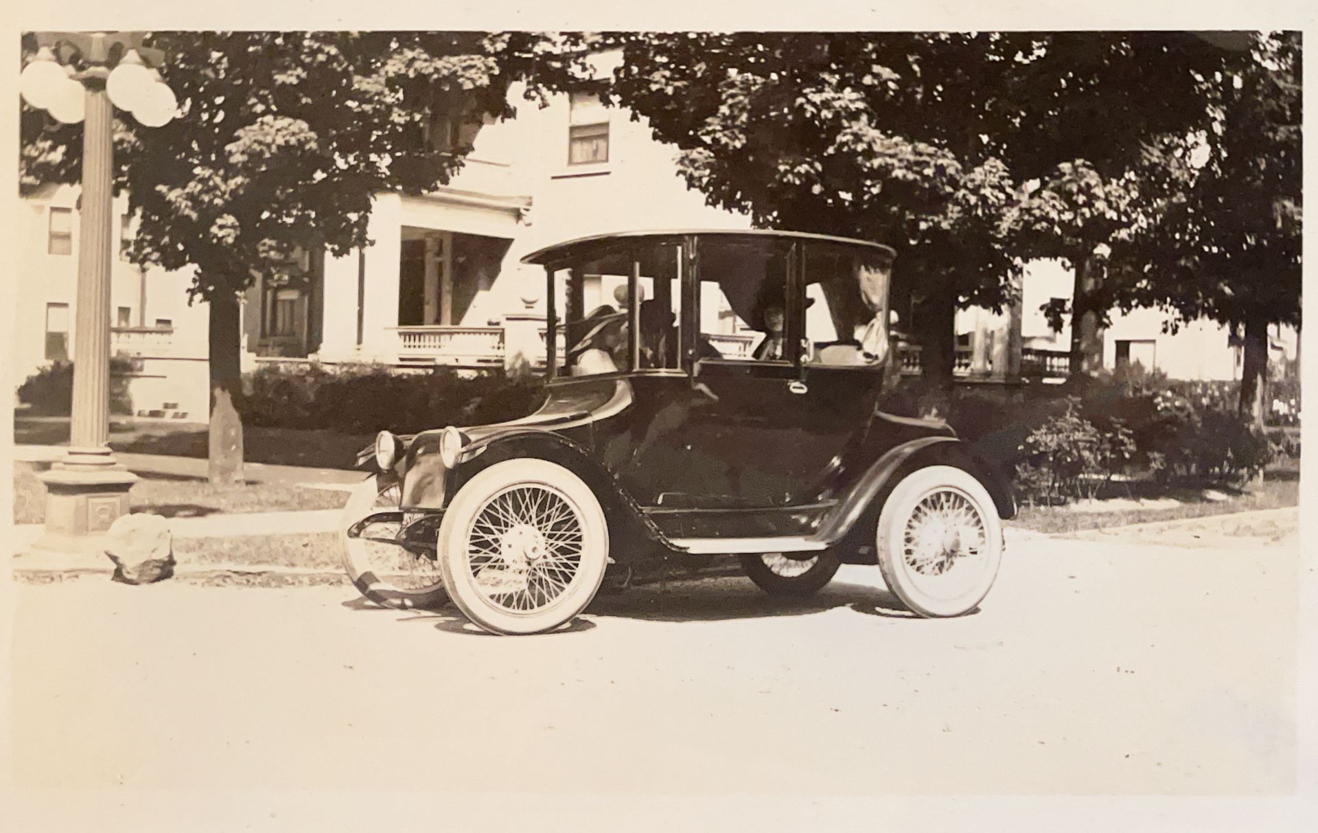 A black and white photo of an old car parked in front of a house
