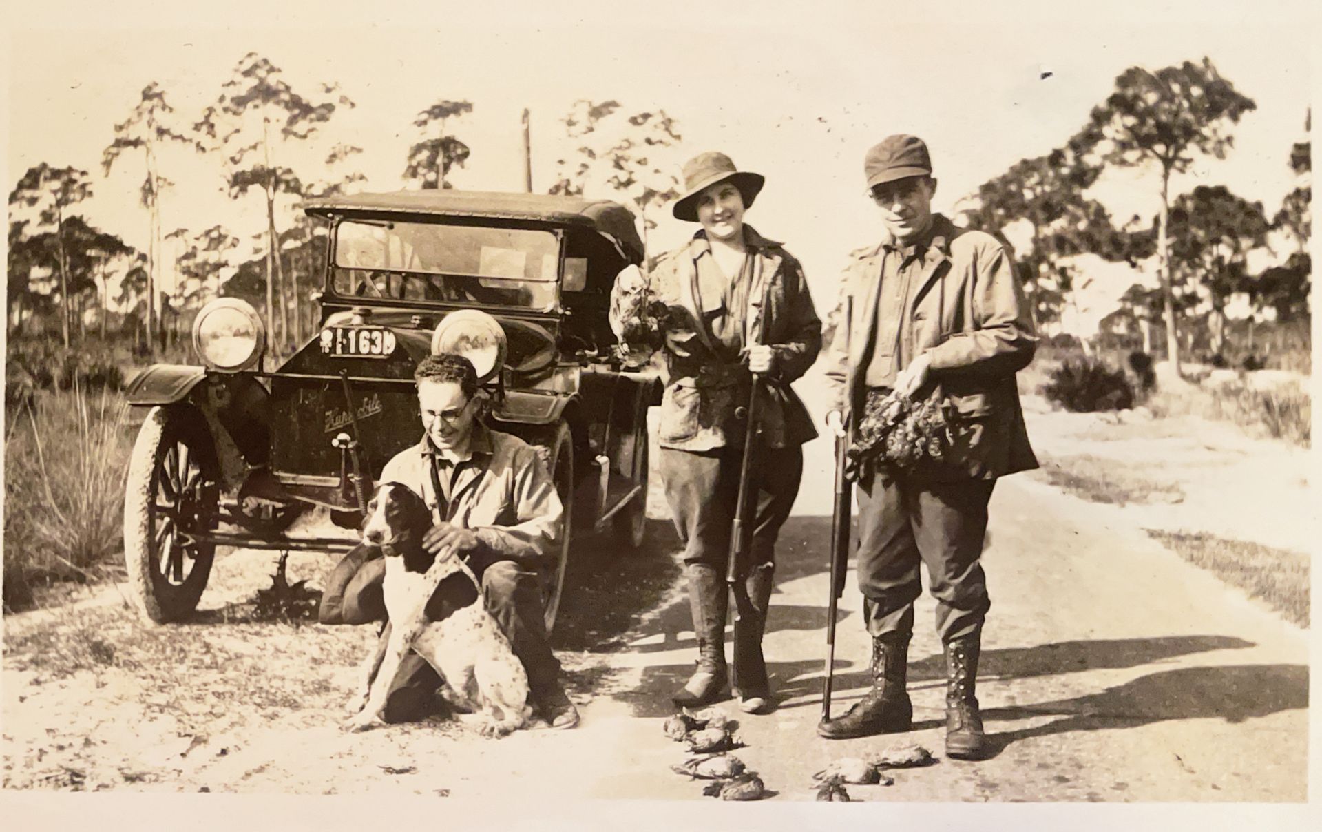 A black and white photo of a group of men standing next to a car