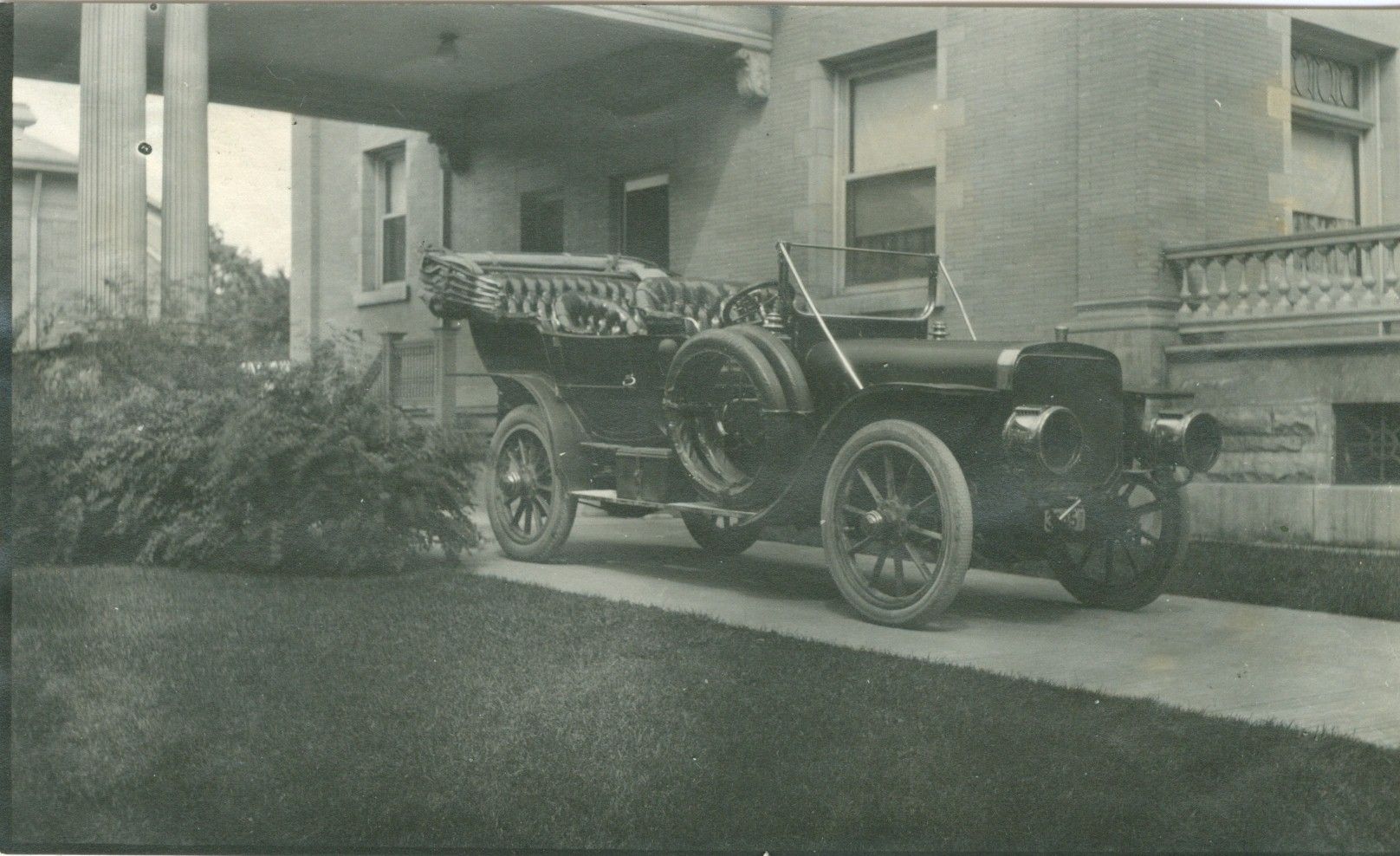 A black and white photo of an old car parked in front of a building