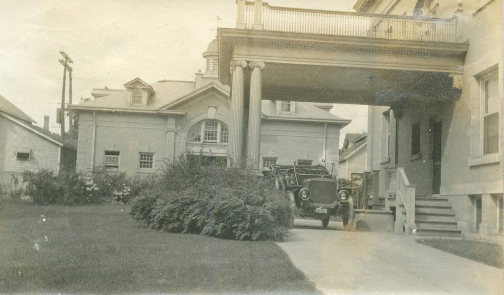 A black and white photo of a large building with a car parked in front of it.