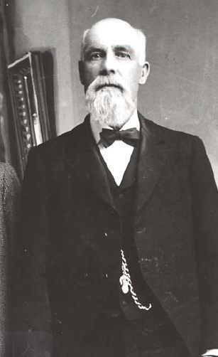 A black and white photo of a man with a beard wearing a suit and bow tie.