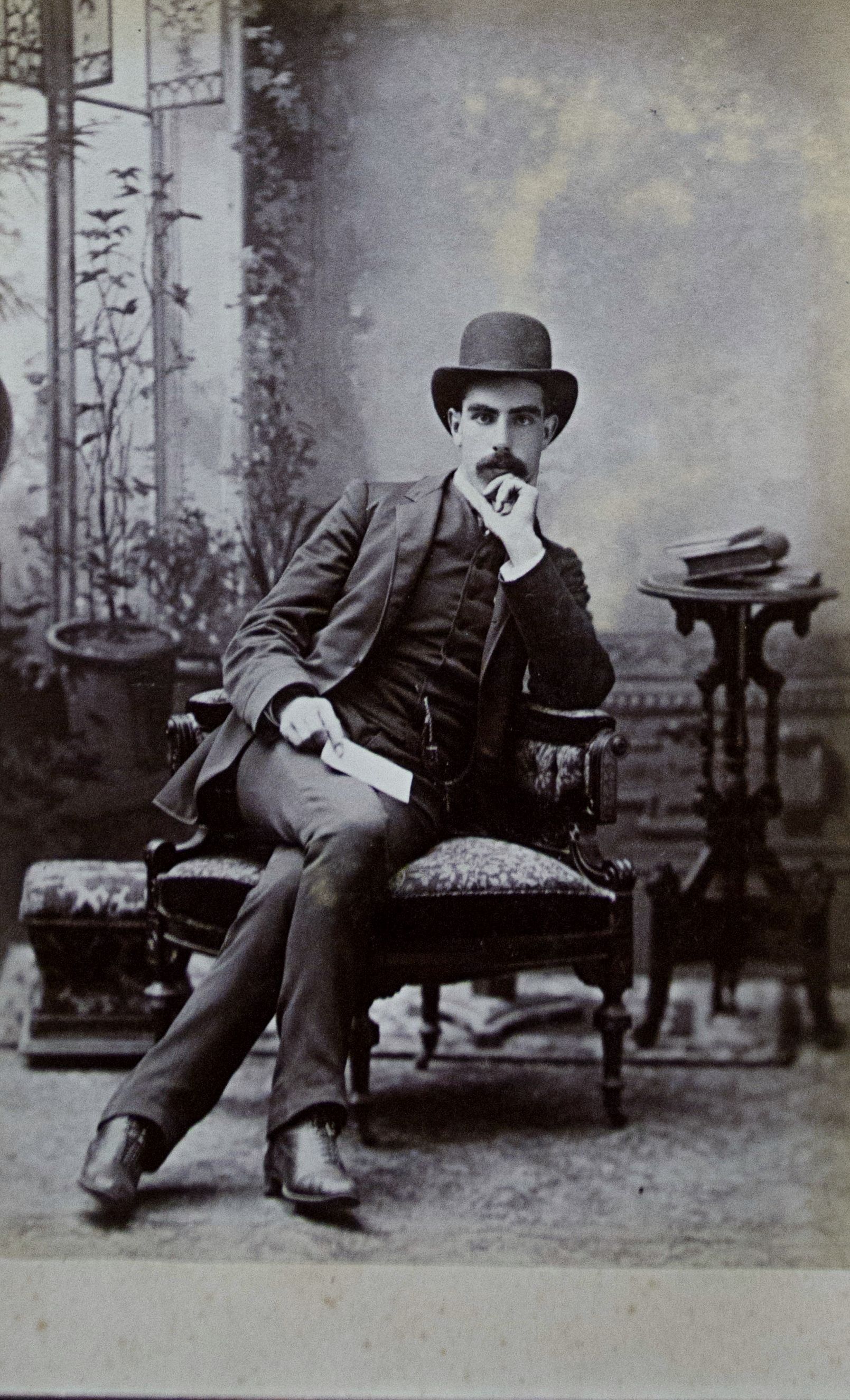 A man in a suit and hat is sitting in a chair