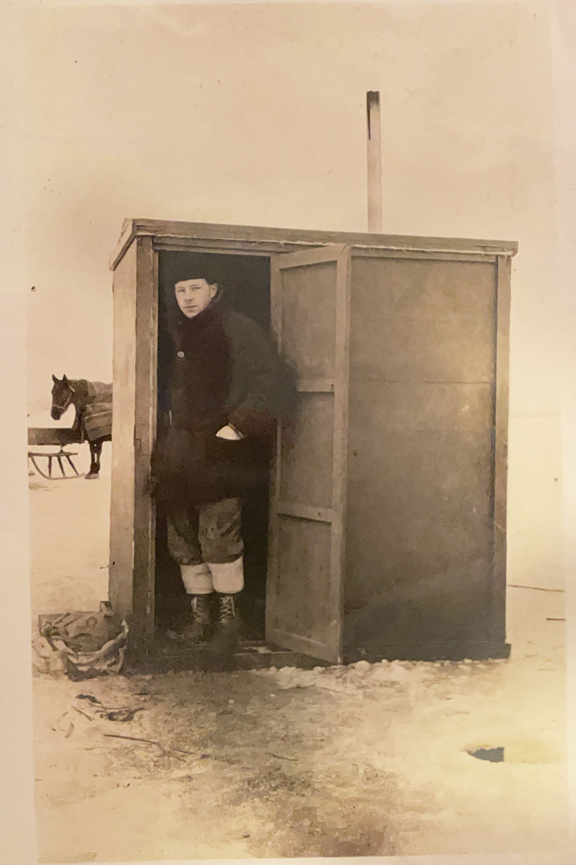 A man is standing in a small wooden building in the snow.