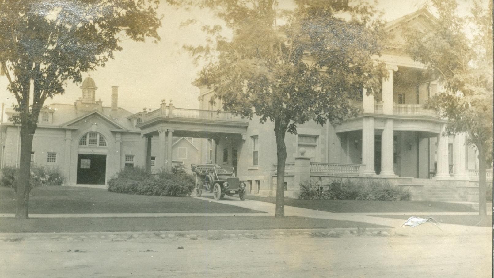 A black and white photo of a house with a car parked in front of it.