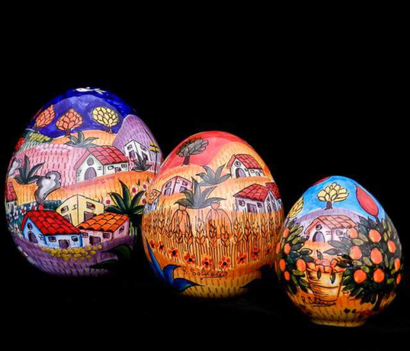 Tre uova in ceramica decorate che raffigurano scene di paesaggi colorati su sfondo nero.