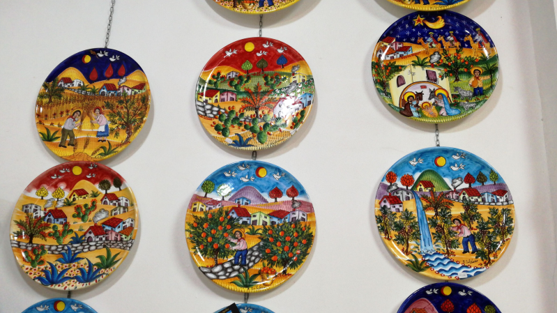 Piatti di ceramica colorati e dipinti raffiguranti scene di vita all'aria aperta, appesi a una parete.