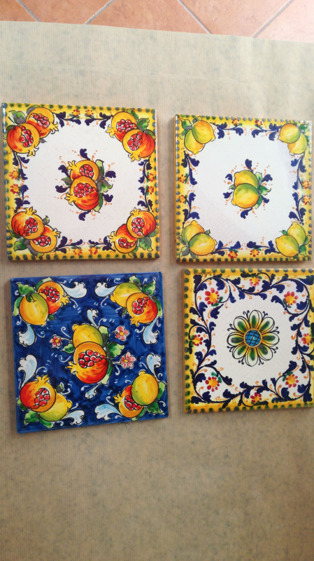 Quattro sottobicchieri quadrati in ceramica con motivi floreali e di frutta.