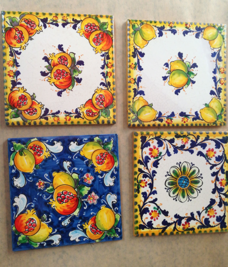 Quattro sottobicchieri quadrati con motivi di frutta: melograni, limoni, bordi floreali.